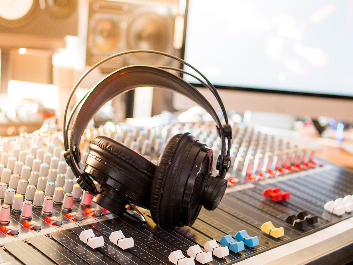 Image of a pair of headphones sitting on a mixing board in a recording studio.