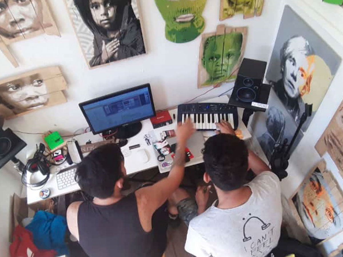 Overhead view of two guys working on beats in a room full of portrait paintings on the walls.